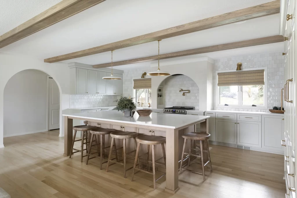 Kitchen with decorative arched doorway and arched stove surround; large center island and natural wood beams on ceiling