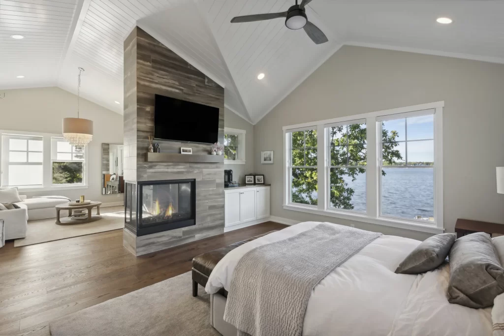 View of master suite that includes fireplace built into wall, white trim, wood flooring, separate seating area and coffee station built into cabinetry. Also includes vaulted ceilings finished in white shiplap